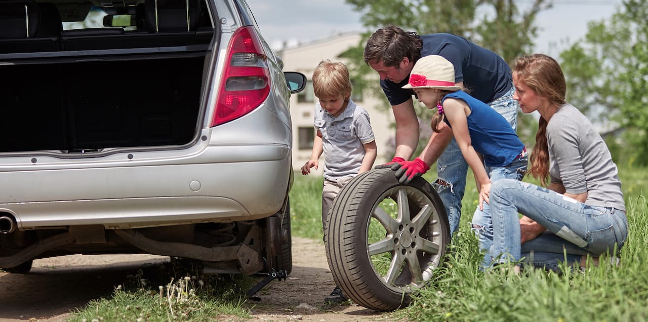 Father and children replacing a tire on the side of a driveway