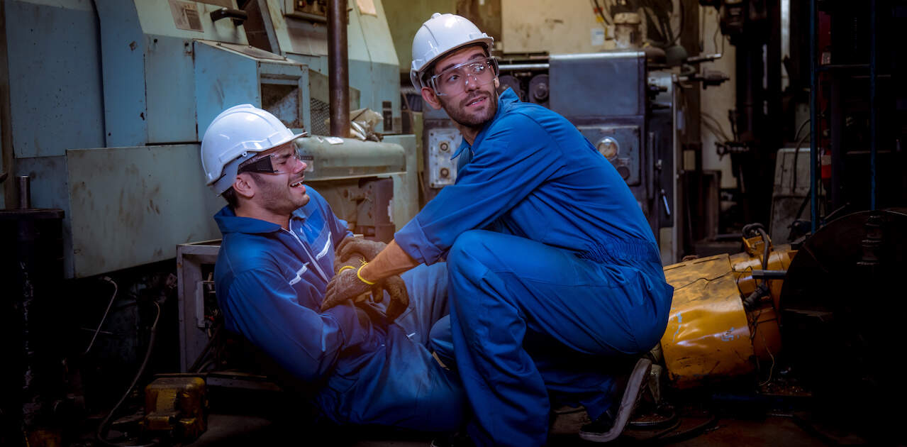 A factory worker helps another worker suffering an injury and emergency