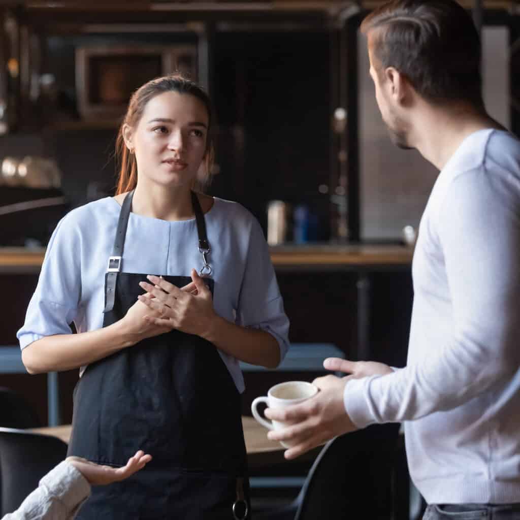 An angry male restaurant customer talks to a young female waitress.