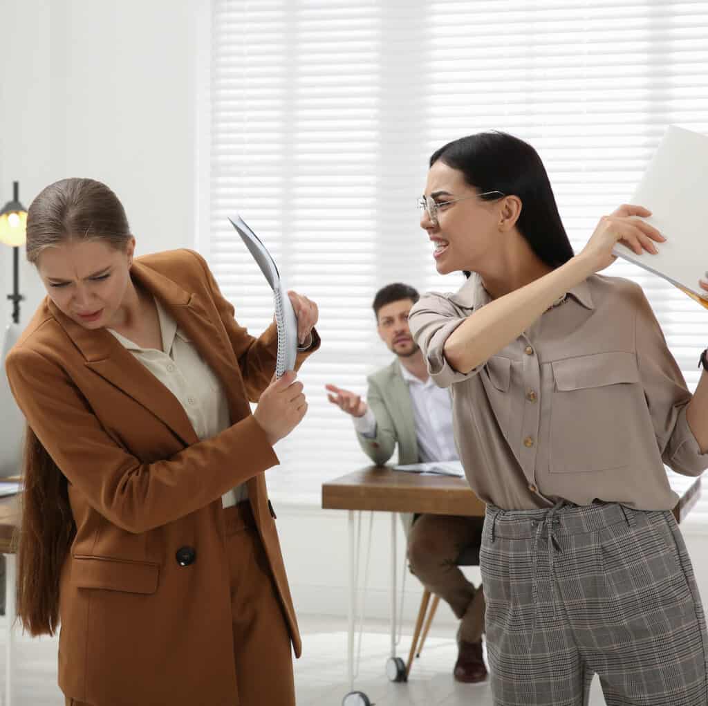 Two female colleagues hitting each other with paper binders.