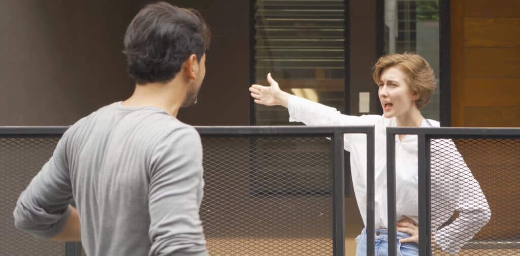 Two adults speaking over a fence with defensive body language