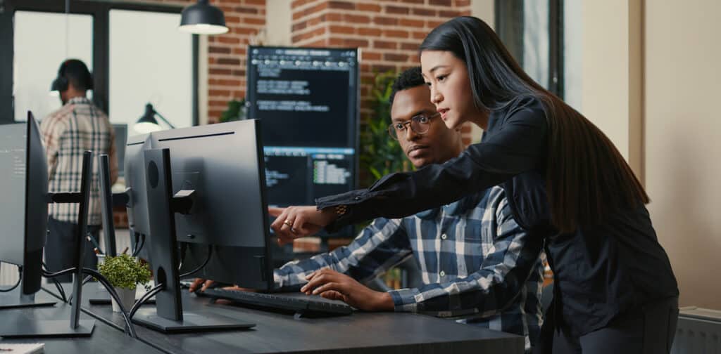 Two programers holding laptop with coding interface walking towards desk and sitting down