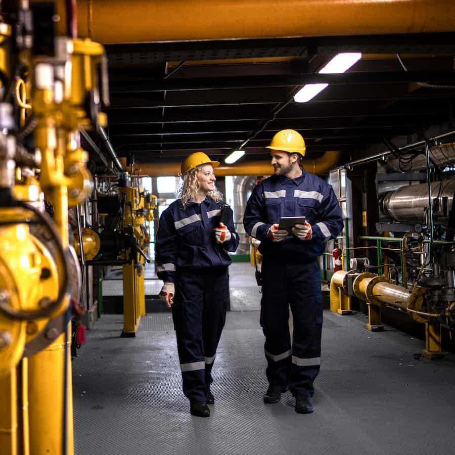 Factory workers in safety equipment walking by gas pipes and checking distribution and consumption.